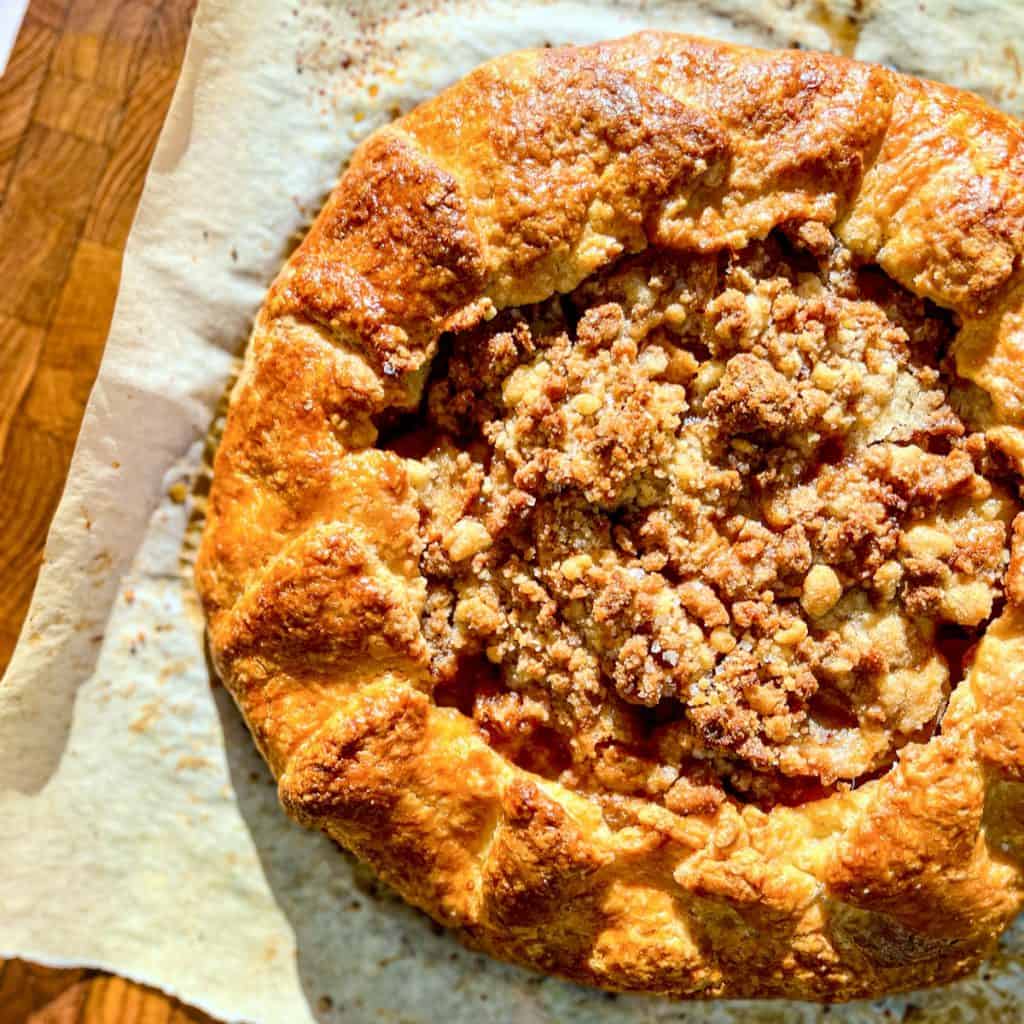An apple streusel galette on a sheet of parchment paper on a cutting board.