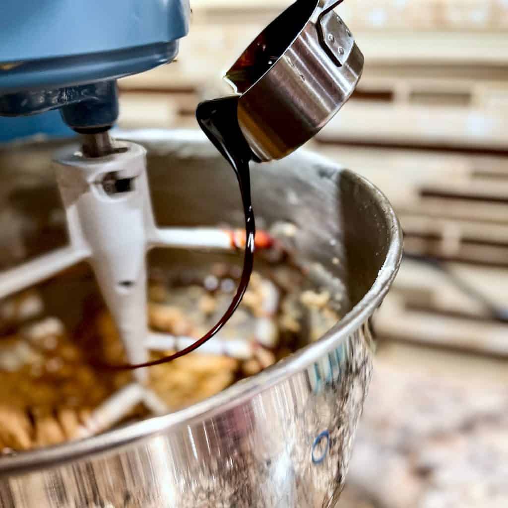 Adding molasses to maple molasses cookie dough in a stand mixer.