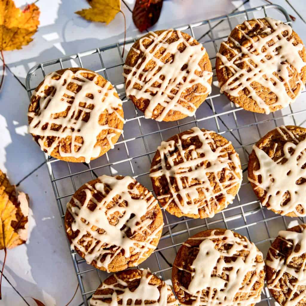 Maple molasses cookies on a wire rack, on a tiled surface, surrounded by fall leaves.