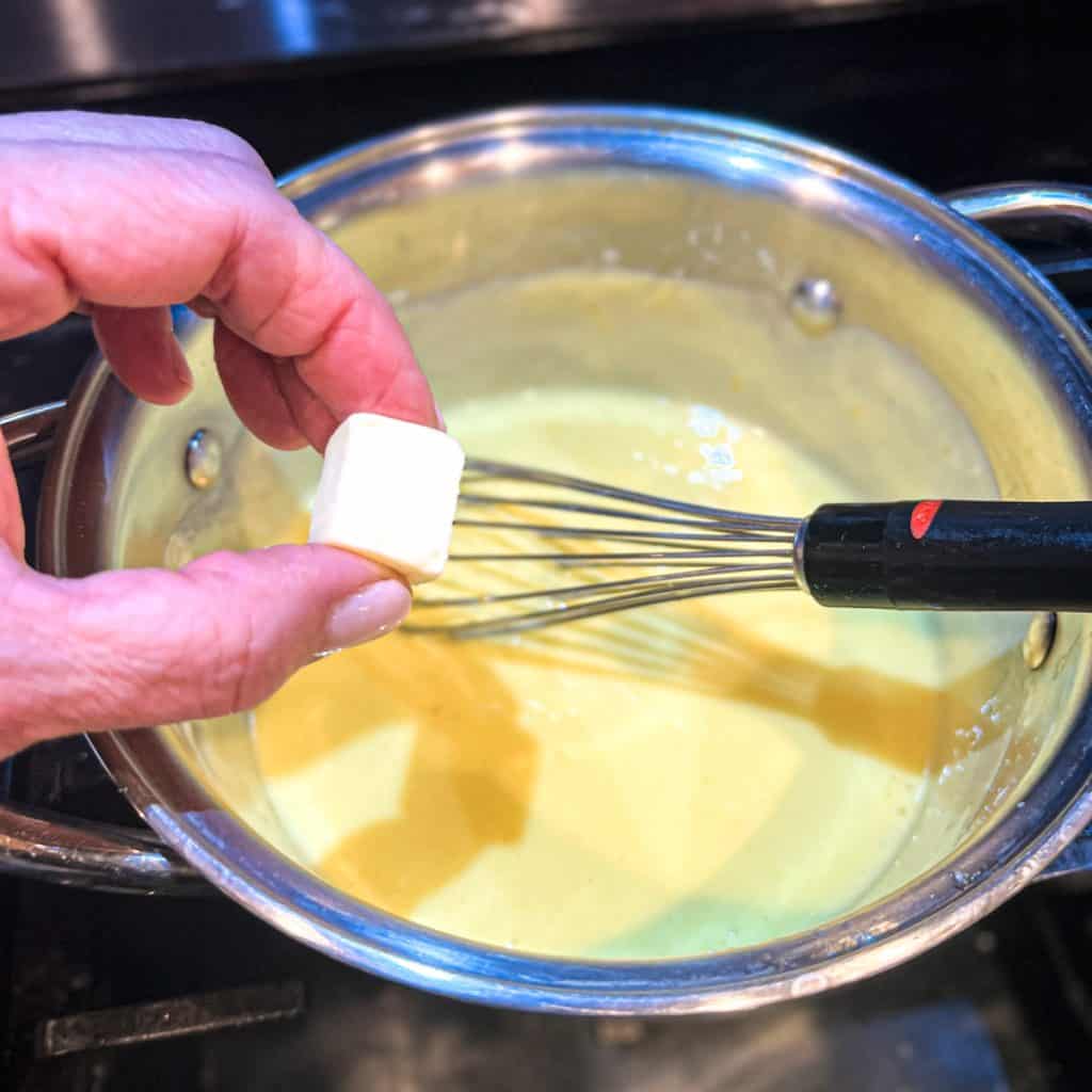 Adding butter to lemon curd in a small saucepan.