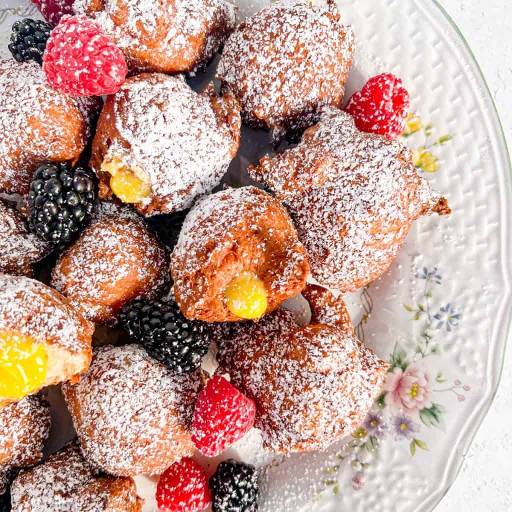 Zeppole and with lemon curd along with fruit on a flowered plate.